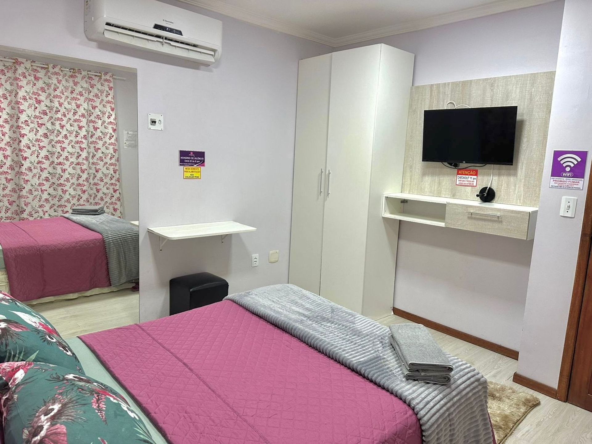 Habitación de hotel con dos camas, un armario, un televisor y un cartel que indica acceso a WiFi.