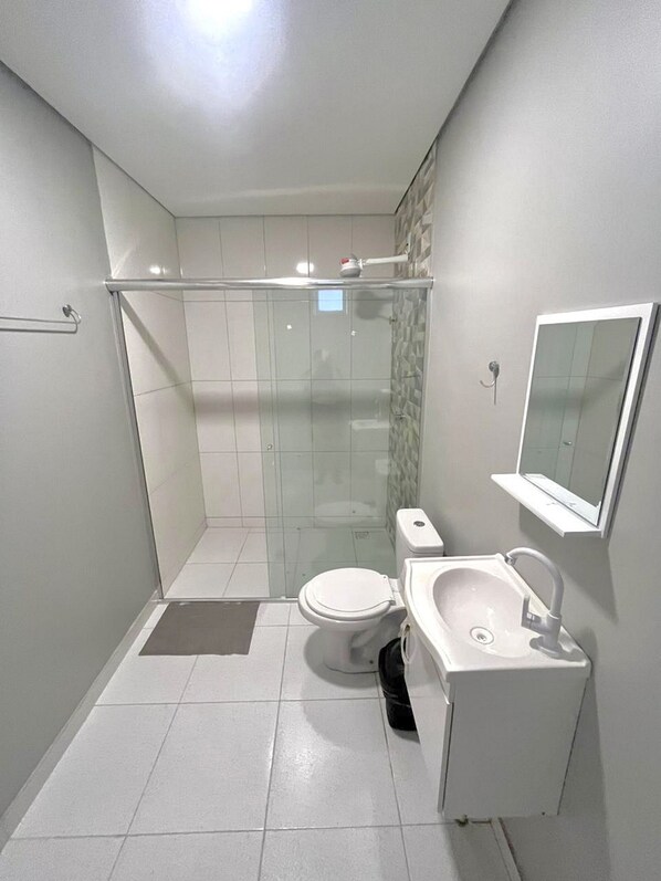 Un baño moderno con cabina de ducha de vidrio, inodoro y lavamanos con espejo.