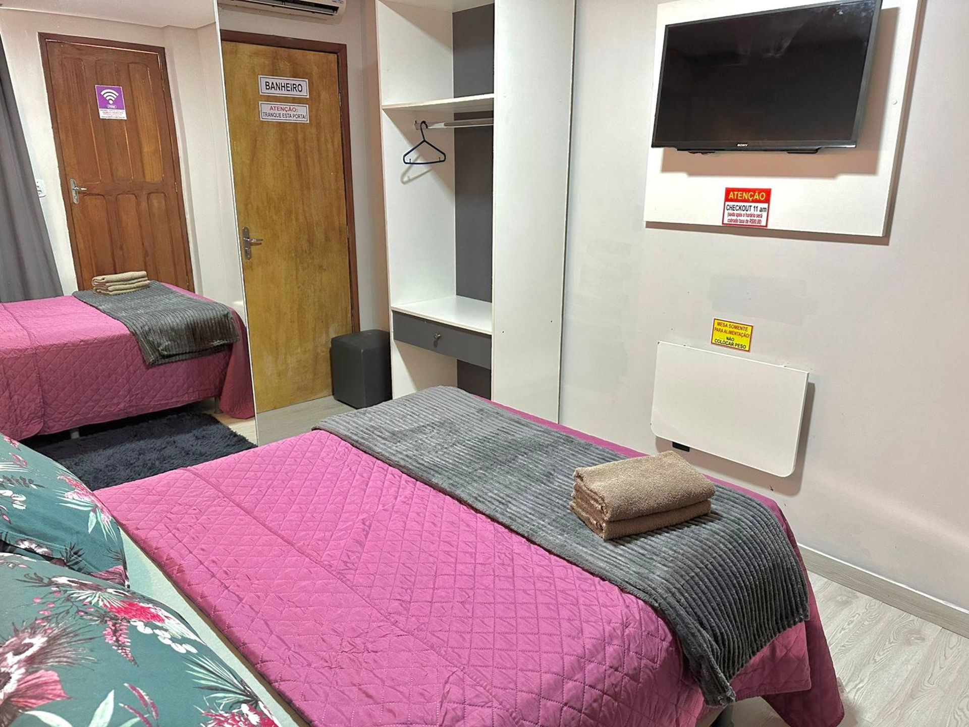 A hotel room with two beds, a TV, and a coat rack.