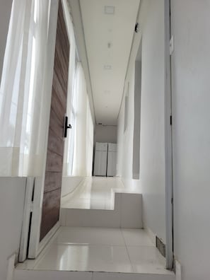 A narrow hallway with a wooden door on the left, a white wall, and a white door on the right. - Hotel Manaus - Dom Pedro (Manaus)