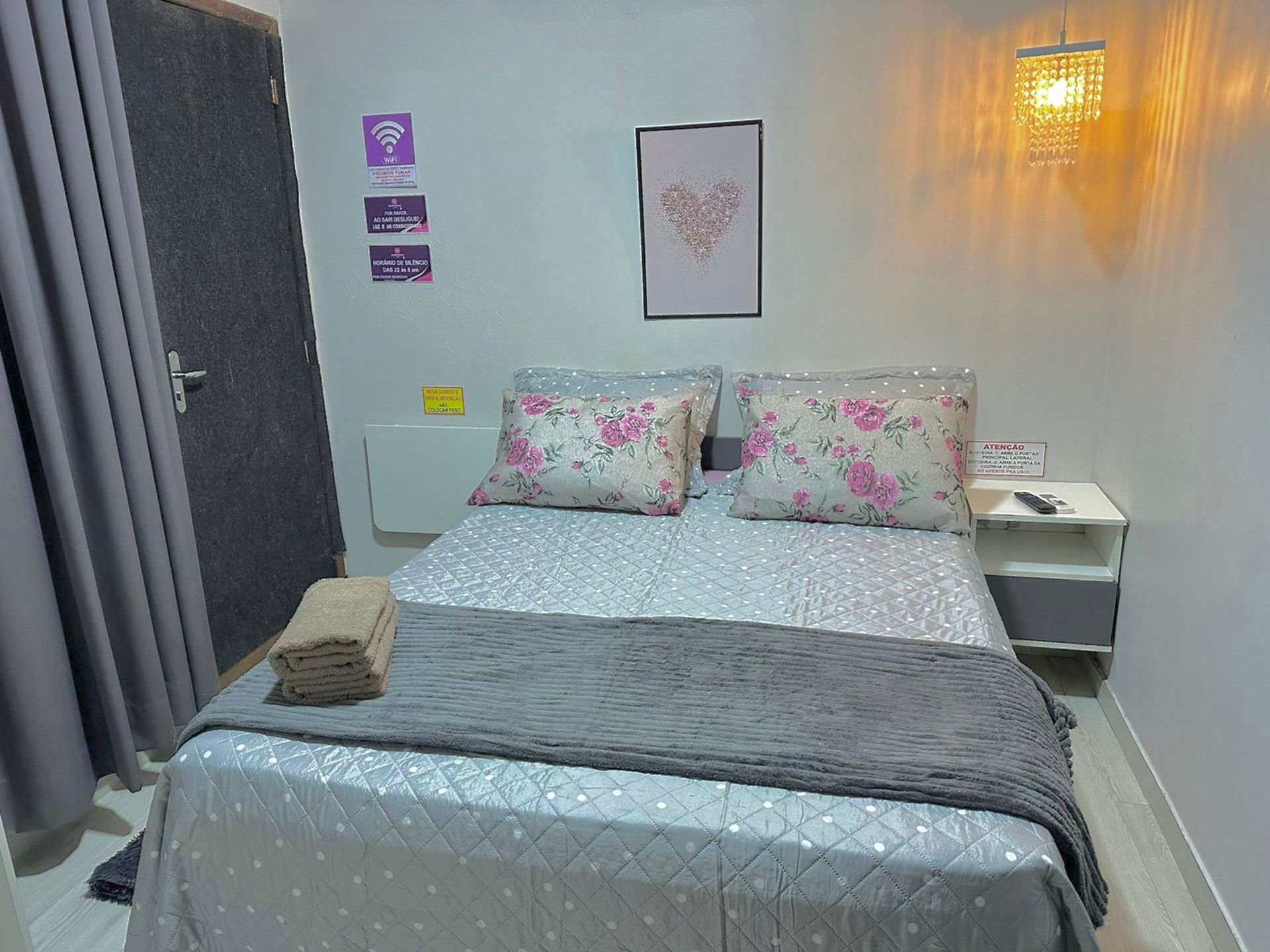 Habitació d'hotel amb llit, tauleta de nit, làmpada penjada a la paret i una porta.