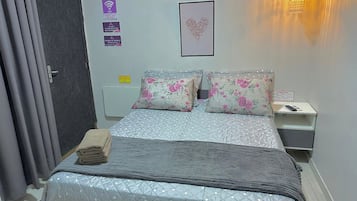 Habitació d'hotel amb llit, tauleta de nit, làmpada penjada a la paret i una porta.