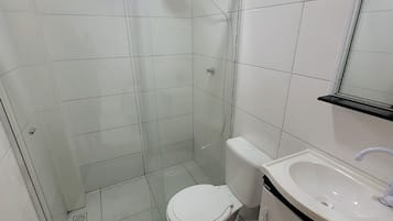 Un baño con ducha acristalada, inodoro y lavamanos con espejo.