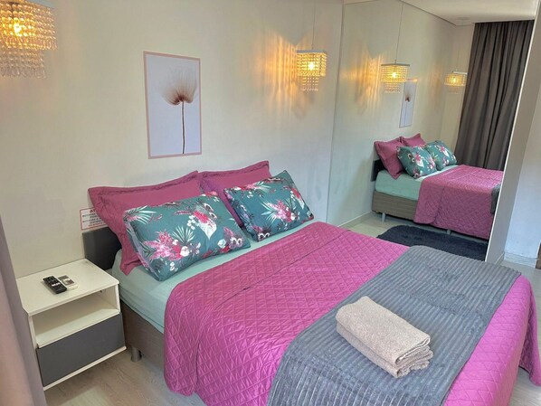 A bedroom with a bed, a nightstand, a mirror, and a wall-mounted light fixture. - Hotel Manaus - Dom Pedro (Manaus)