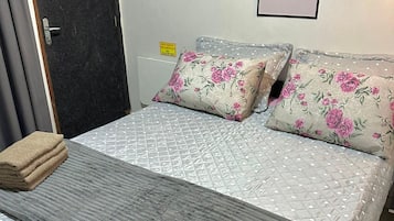Cama bem arrumada com colcha cinza, duas almofadas florais e manta cinza.