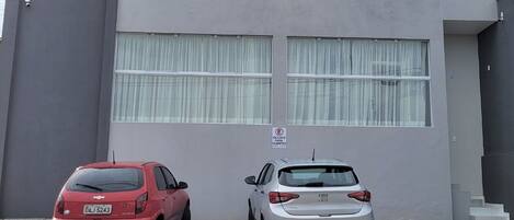 A parking area with two cars parked in front of a building with large windows and a sign indicating a reserved parking space.