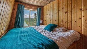 A wooden-paneled room with a bed, curtains, and a window overlooking greenery. - Der Kastle Ski Condo · Schweitzer Retreat Comfort for all Prime location (Sandpoint)