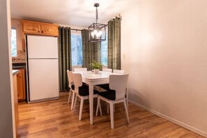 Cozy dining area with a round table and six chairs, featuring a stylish chandelier and kitchenette.