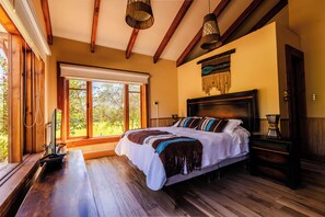 A bedroom with a large bed, wooden floor, and a window with a view of trees. - REFUGIO EL MOLLE (Vicuña)