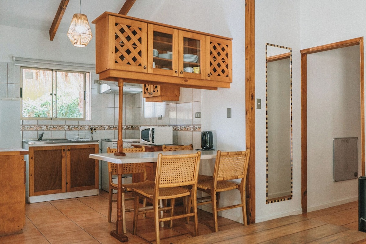 A kitchen with wooden cabinets, a dining table with chairs, a stove, and a window.