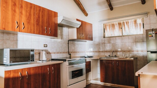 Una cocina con armarios de madera, microondas, horno y una ventana con cortinas.