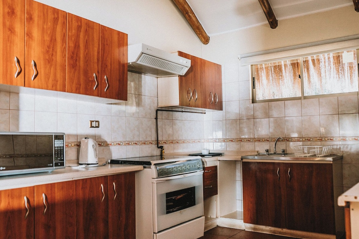 A kitchen with wooden cabinets, a microwave, an oven, and a window with curtains.
