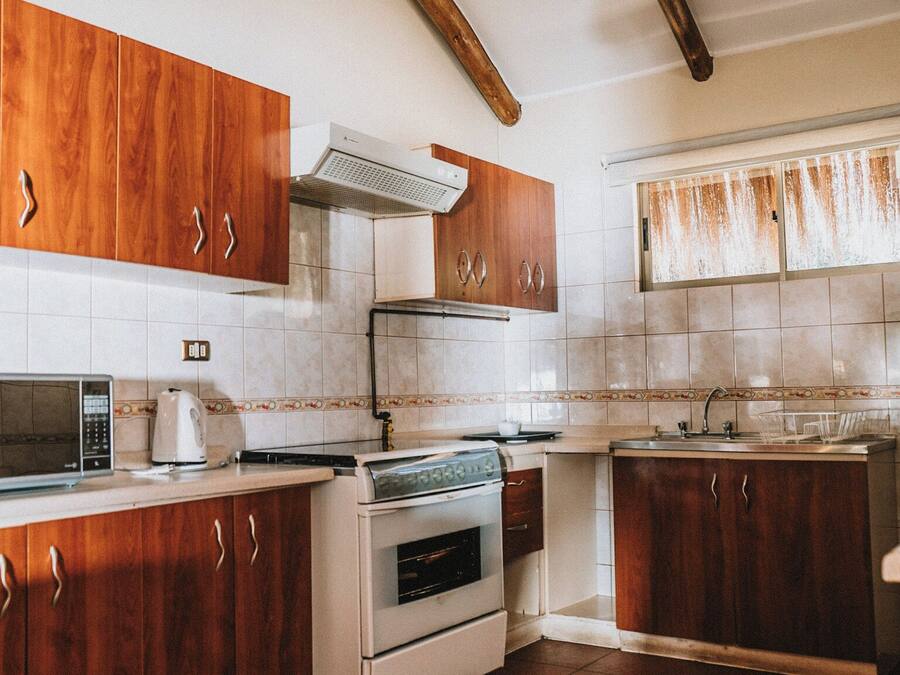 Cozinha com armários de madeira, micro-ondas, forno e janela com cortinas.