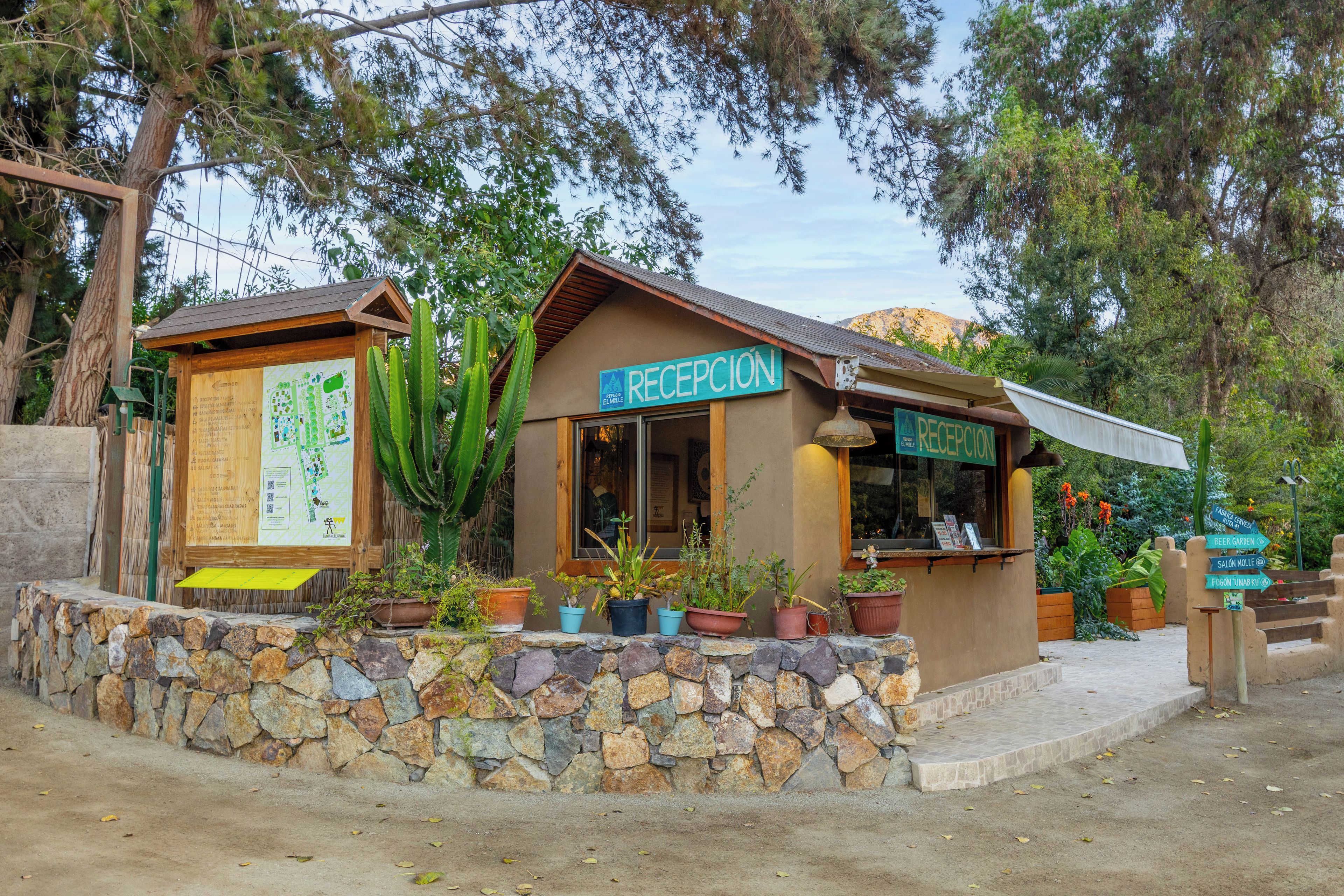 Un área de recepción con un cartel, plantas en macetas y una pared de piedra.