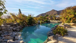 Una piscina cristalina rodeada de rocas y vegetación, con una montaña al fondo.