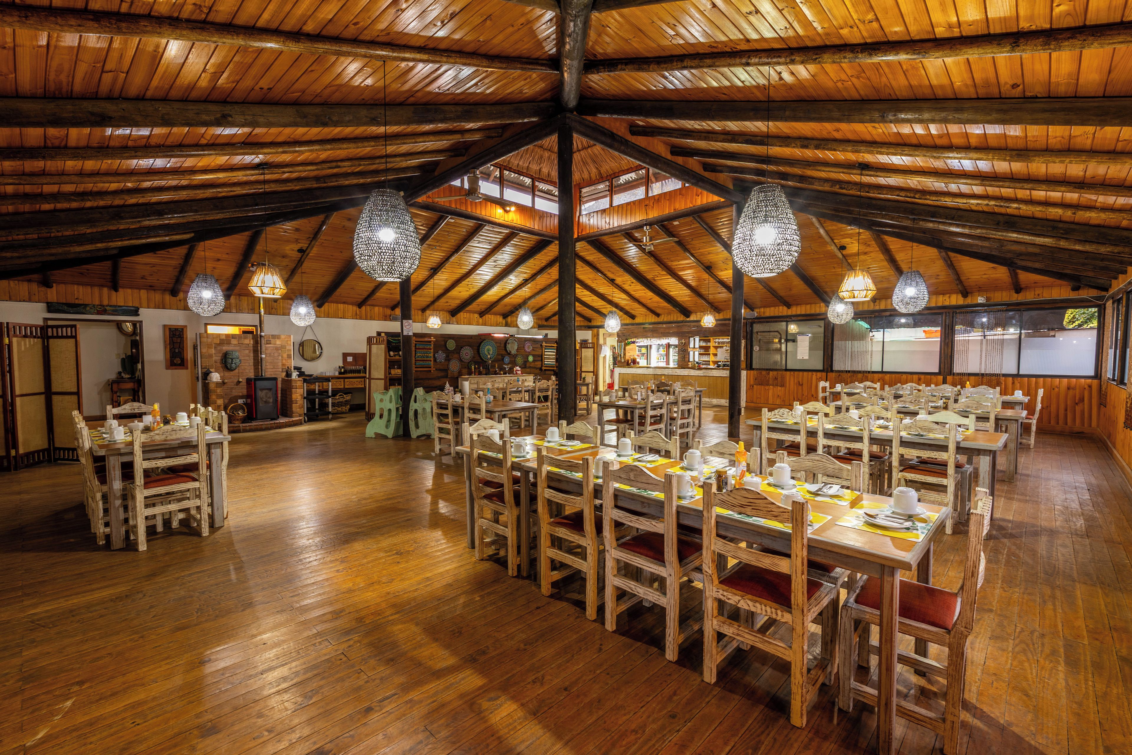 Un comedor amplio con mesas y sillas de madera, un techo alto de madera y lámparas colgantes.