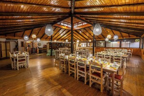 Un comedor amplio con mesas y sillas de madera, un techo alto de madera y lámparas colgantes.