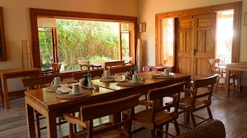 Un comedor con mobiliario de madera, ventanas amplias y vistas a la vegetación exterior.