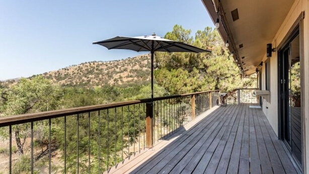 Eine Holzterrasse mit Metallgeländer, einem Sonnenschirm und Blick auf eine hügelige Landschaft.