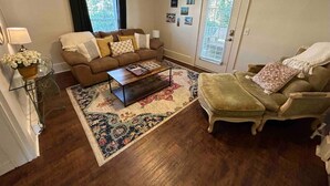 Un salon avec un canapé marron, un fauteuil vert, une table basse et un tapis à motifs.