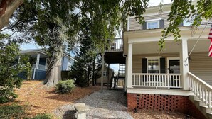 Une maison à deux étages avec un porche à l’avant, un banc en pierre et un chemin de gravier menant à l’entrée.