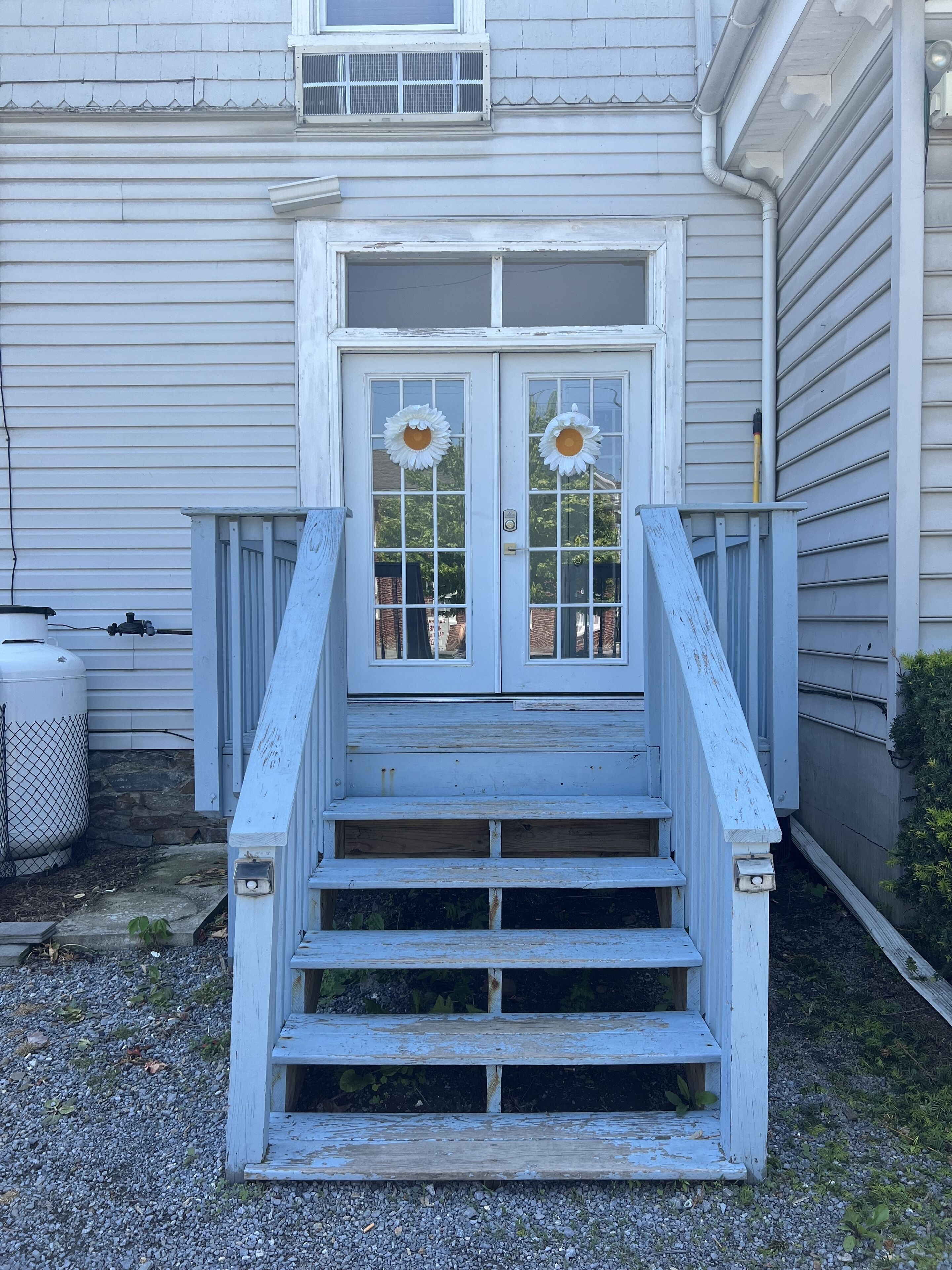 A house with a front porch, a set of stairs leading to a double door with glass panels, and a small window above the door.