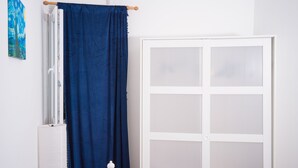 Ein Zimmer mit einer weißen Tür, einem Fenster mit blauem Vorhang und einem weißen Heizkörper.