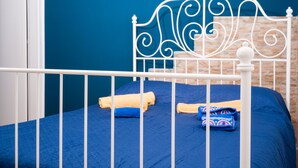 Ein Bett mit weißem Metall-Kopfstück, einer blauen Matratze und einer blauen Wand im Hintergrund.