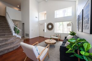 A spacious living room with a staircase, a round wooden coffee table, a sofa, and a large green plant.