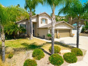 A two-story house with a garage, surrounded by palm trees and well-maintained landscaping.