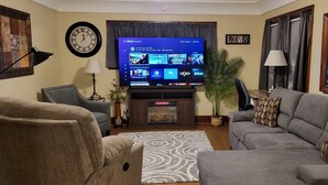 A living room with a large flat-screen TV, a clock, a couch, a chair, and a decorative wall piece. -  Oak Street Retreat  (Menasha)
