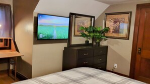 A bedroom with a bed, a desk with a lamp, a TV on the wall, and two framed pictures. -  Oak Street Retreat  (Menasha)
