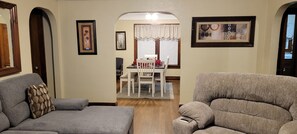 A living room with two grey sofas, a dining table with chairs, and a hallway leading to a dining area. - Oak Street Retreat (Menasha)
