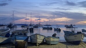 Ein Yachthafen mit mehreren vertäuten Booten, ruhigem Meer und einem Sonnenuntergang im Hintergrund.