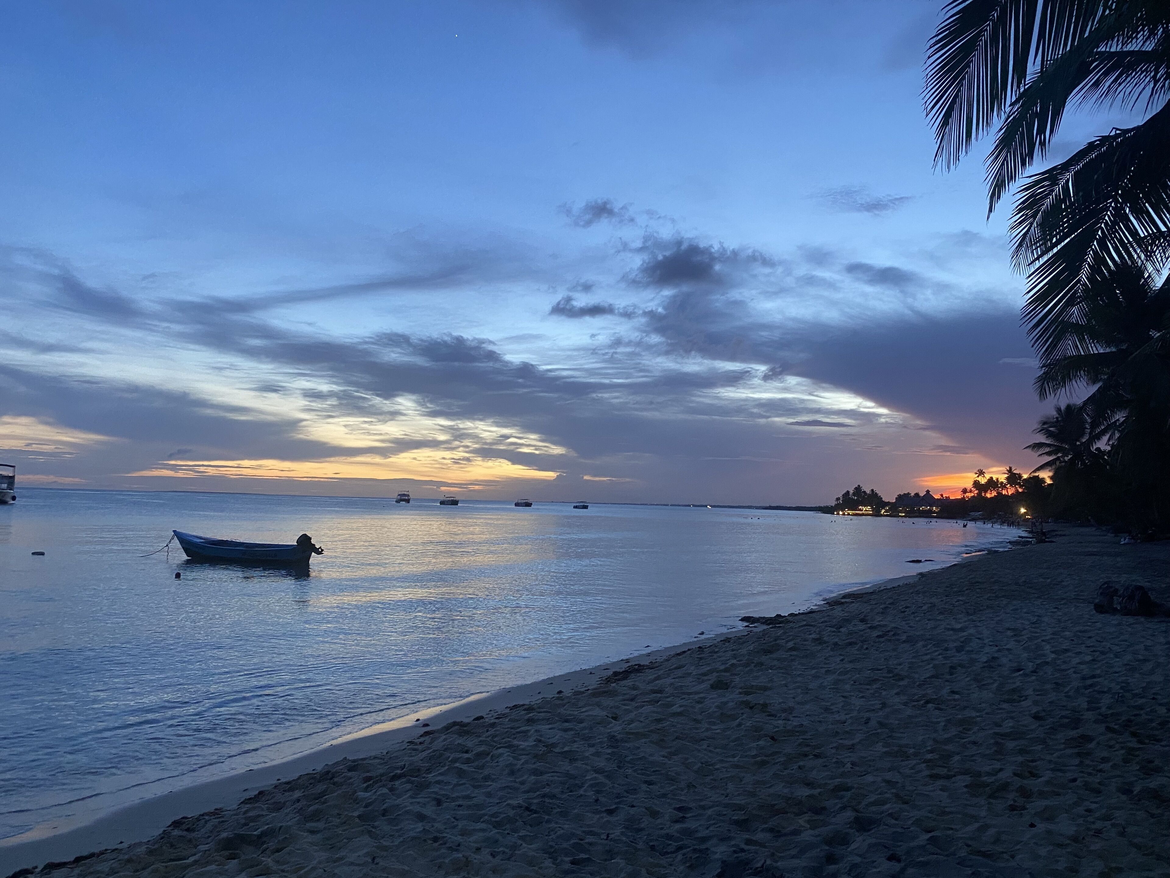 A beach with calm waters, a boat, and a sunset.
