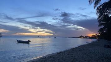 A beach with calm waters, a boat, and a sunset.