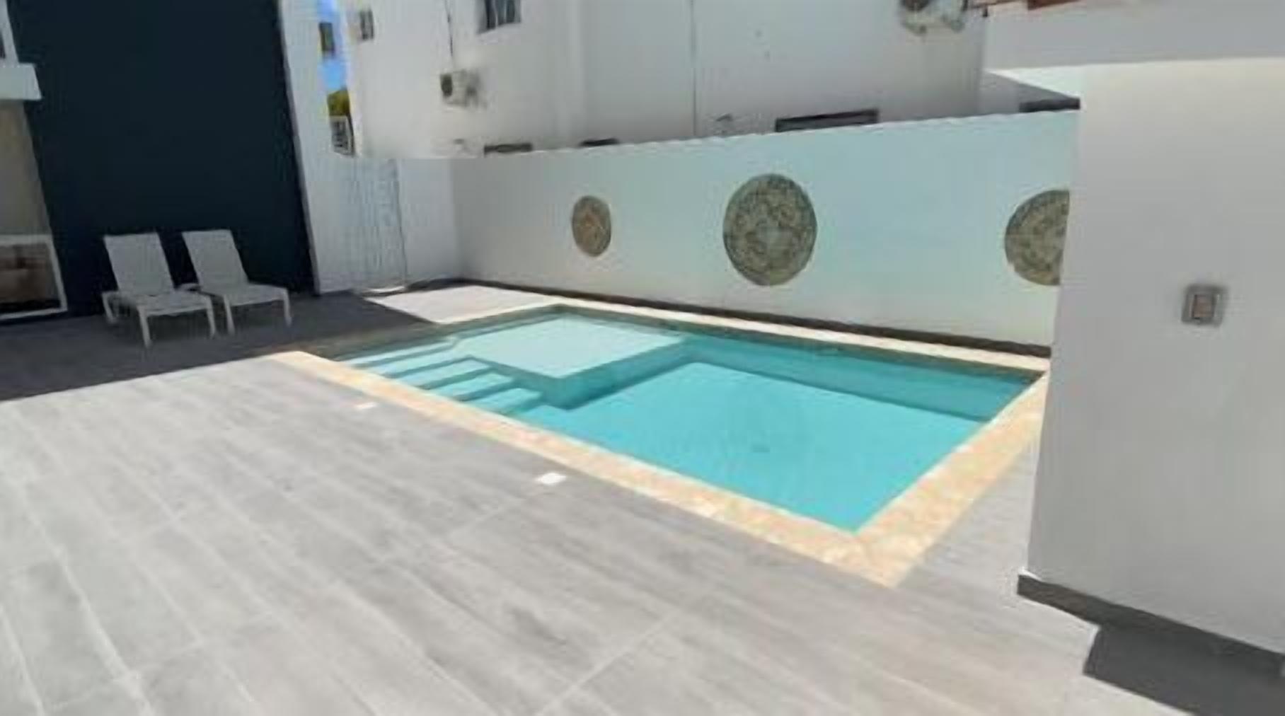 A swimming pool with a tiled deck, surrounded by a white building with circular decorative elements on the walls.