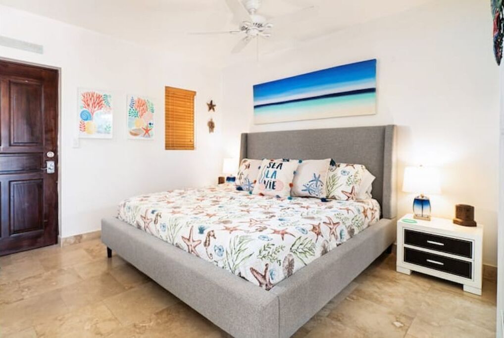 A bedroom with a bed, a nightstand, a ceiling fan, and artwork on the walls.