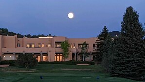 Un edificio grande con varios pisos, un césped bien cuidado y una luna visible en el cielo.