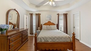 A bedroom with a wooden bed, a dresser, a ceiling fan, and a large mirror. - Full Home on Sunstone with fast WiFi and easy access. (Lafayette)