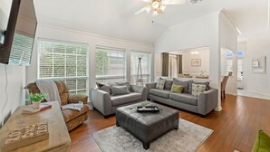 A spacious living room with a large ceiling fan, two grey sofas, a coffee table, and a wooden side table with a plant. - Full Home on Sunstone with fast WiFi and easy access. (Lafayette)
