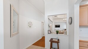 A hallway with a wooden floor, white walls, a mirror, and a small table with a book and a plant. - Full Home on Sunstone with fast WiFi and easy access. (Lafayette)