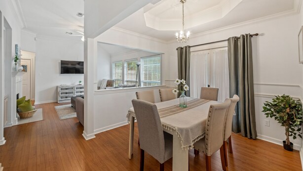 A dining area with a table set for six, surrounded by chairs, a chandelier, and a view of a living room with a television. - Full Home on Sunstone with fast WiFi and easy access. (Lafayette)