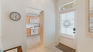 A hallway leading to a kitchen with wooden cabinets, a white stove, and a clock on the wall. - Full Home on Sunstone with fast WiFi and easy access. (Lafayette)