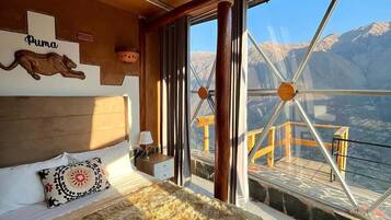 A room with a large bed, a wooden ceiling, a window with a view of mountains, and a sign with the word "Puma".