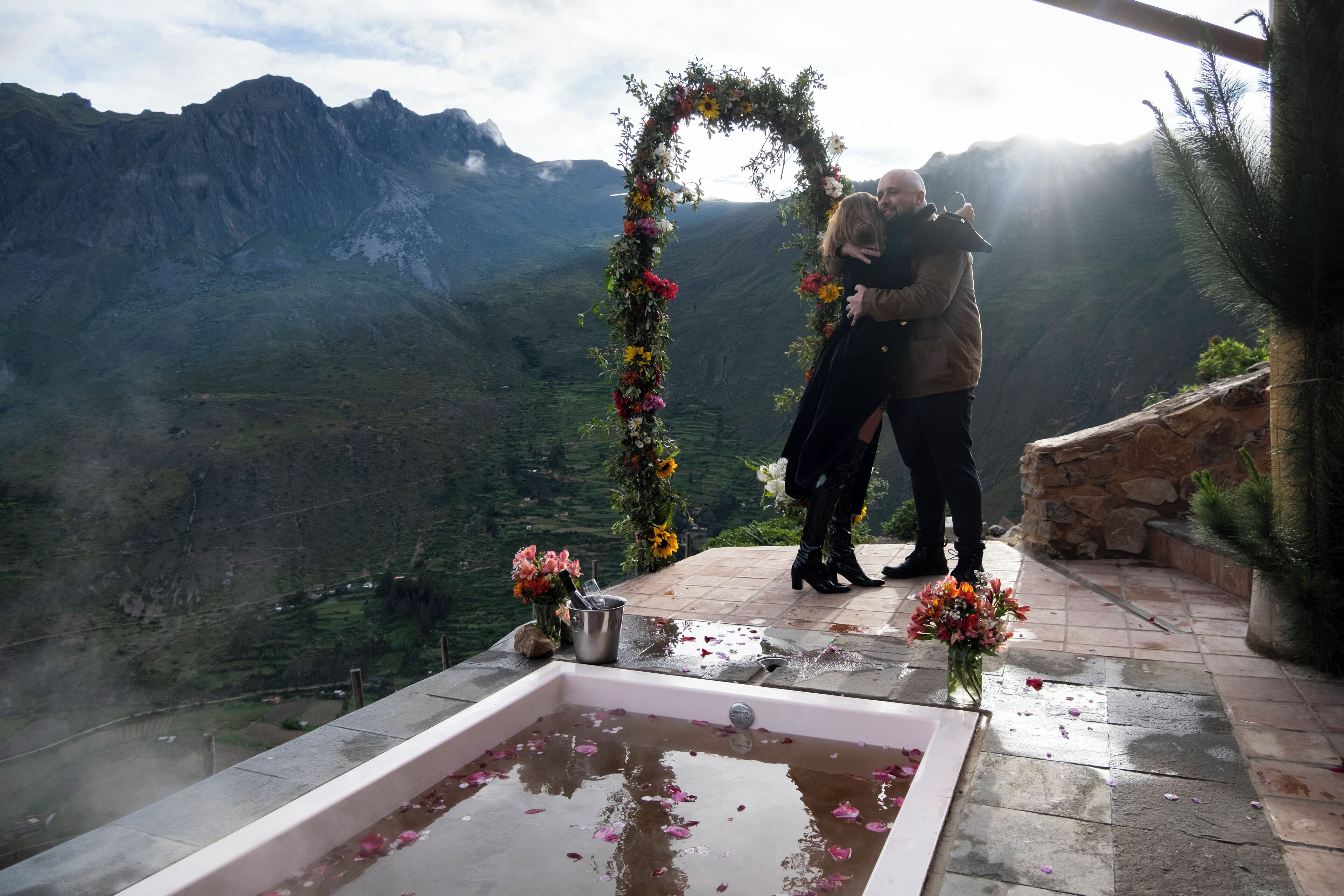 Una coppia si abbraccia sotto un arco fiorito con montagne sullo sfondo.