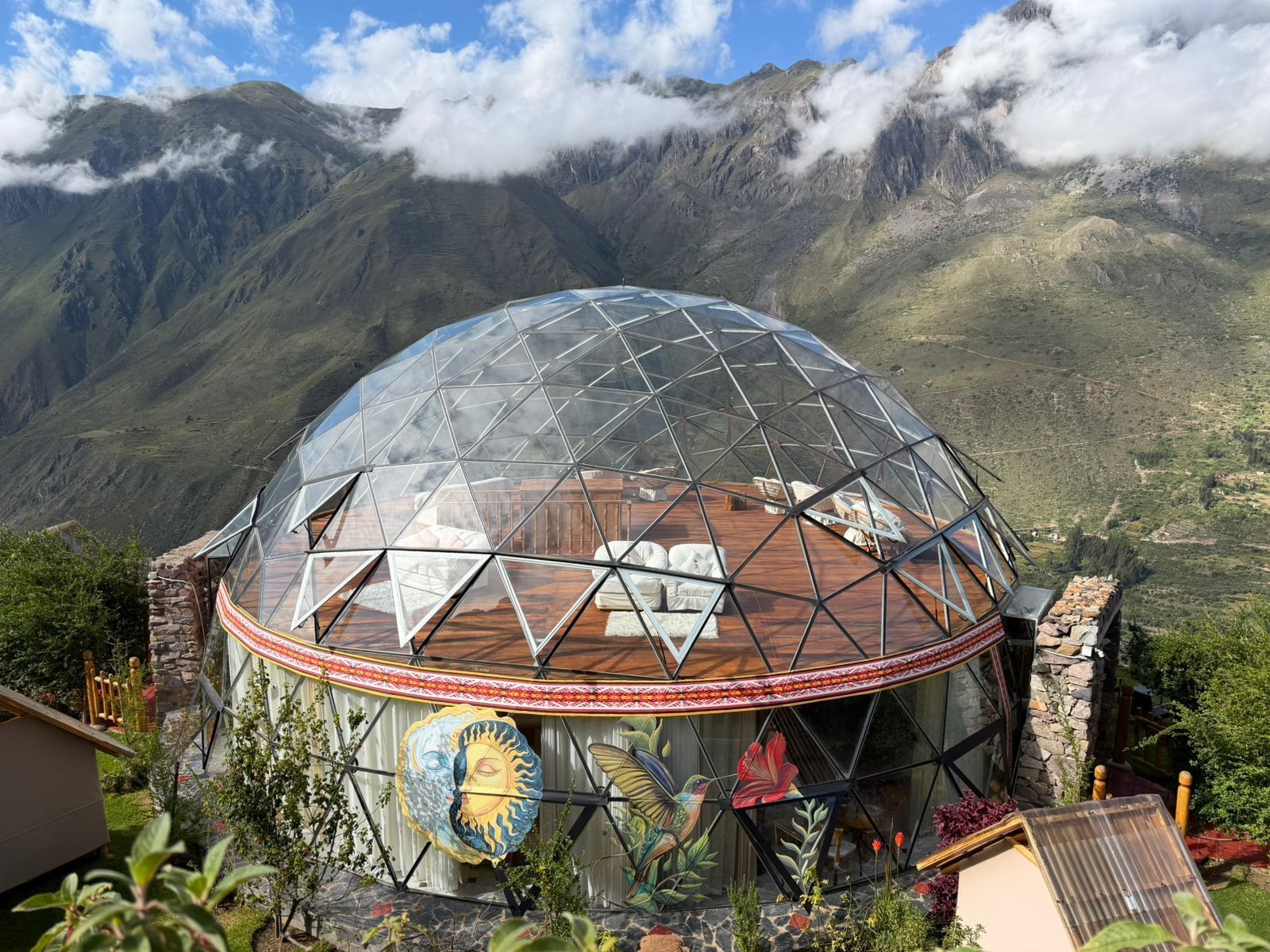 Una estructura de cúpula geodésica con terraza de madera y un mural de un sol y un pájaro.