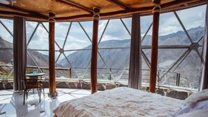 Una habitación con una cama grande, una mesa con sillas y vistas a montañas a través de amplios ventanales.
