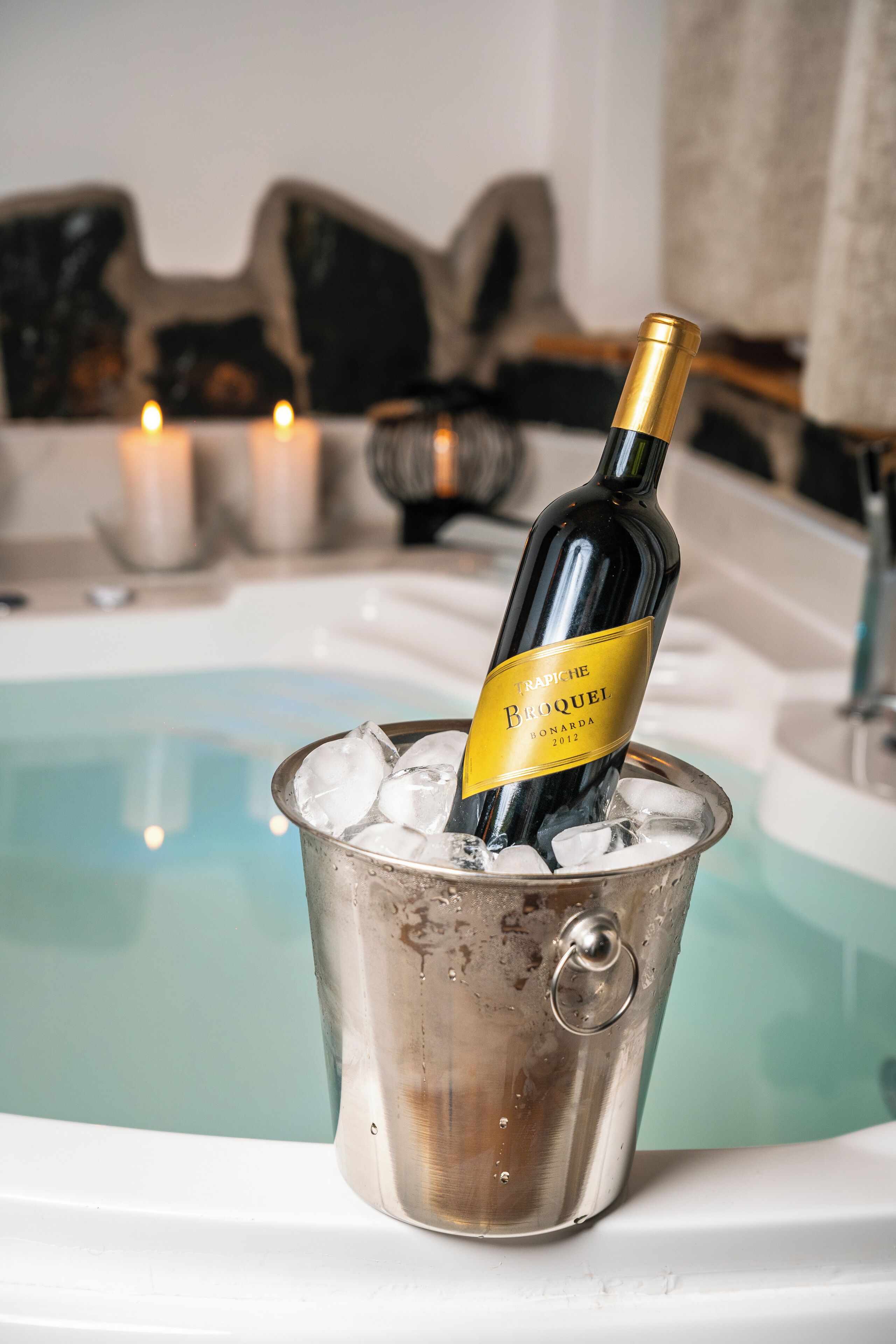Una botella de vino en un balde metálico con cubitos de hielo, cerca de una piscina.