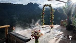Un banco de piedra con un jacuzzi, rodeado de niebla y flores, con vistas a un paisaje montañoso.